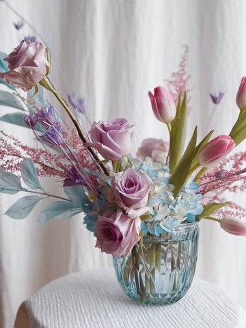A blue glass vase with cool pastel flowers