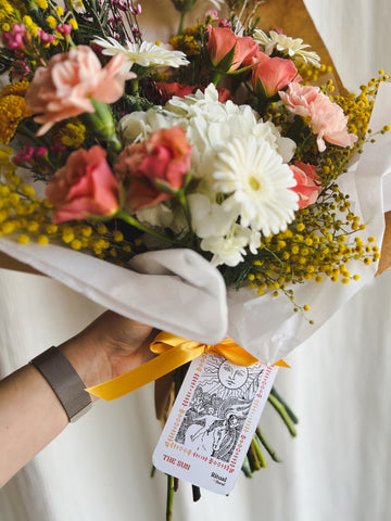 A warm pastel bouquet of flowers with a The Sun tarot card
