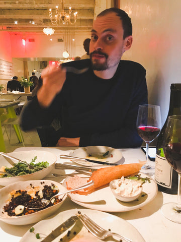 A man sitting at a table at a restaurant with a glass of wine and plate of food.