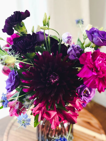 A small vase arrangement with dark purple, magenta, and blue flowers