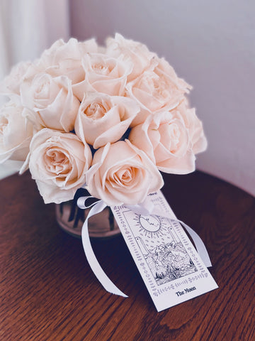 A small arrangement of white roses with a The Moon card tied to the vase with ribbon