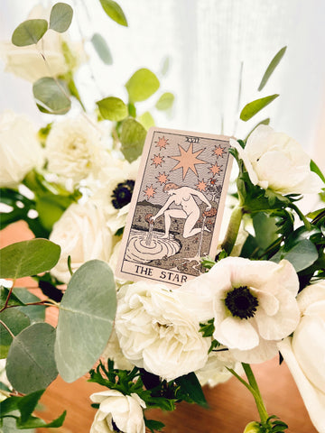 The Star tarot card sitting atop a flower arrangement with white anemones and eucalyptus