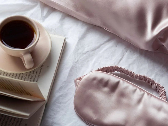 Pink Liv Lindley Sleep Set on bed next to a mug  of a hot drink, eye mask displayed near silk pillowcase