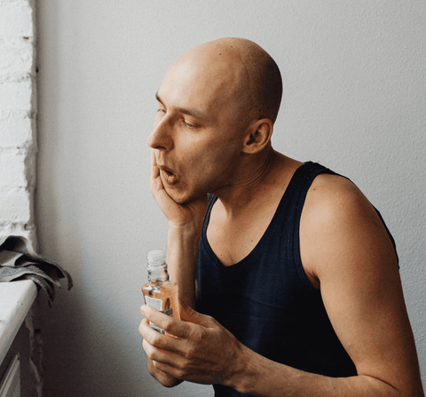 man in black tank top applying after shave to his face in the bathroom