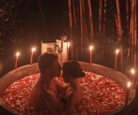 couple bathing in a small outdoors tub with rose petals and candles on valentine's day