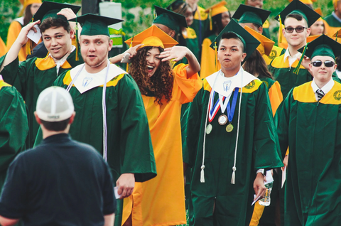 photo of students in green and yellow caps and gowns celebrating graduation