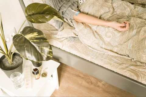Natural interiors. Woman in bed with a drip in her arm, next to a bedside table with a potted plant on top.