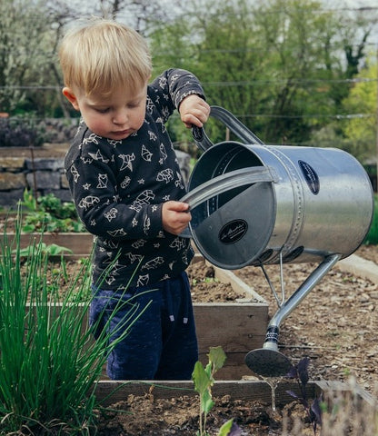 Toddler watering plants outdoors.