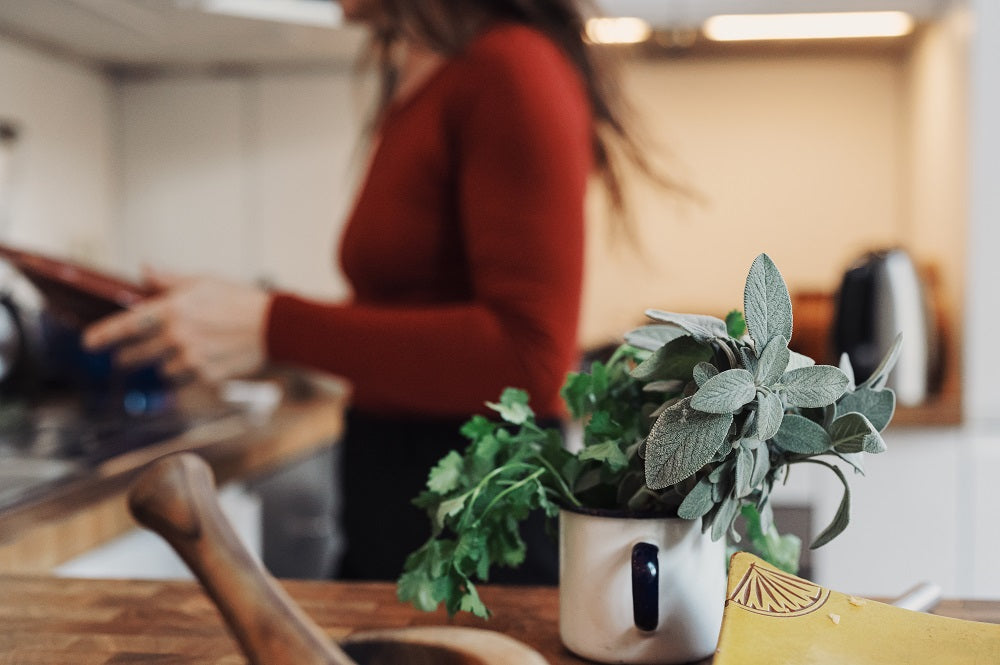 Herbs on a kitchen table with woman in the background.