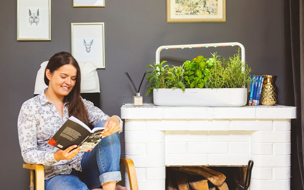 Smart Garden 9 on a fireplace with a woman sitting in a chair beside it.