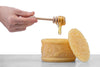 hand dripping honey from a wooden dipper into moulded beeswax honey pot