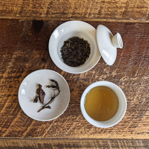 three white dishes against wood holding gabacha oolong wet leaves, dry leaves, and brewed tea