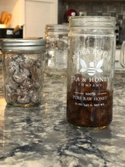 A mason jar with uncooked boba pearls sits on a marble kitchen counter next to a honey jar with cooked boba in a simple syrup