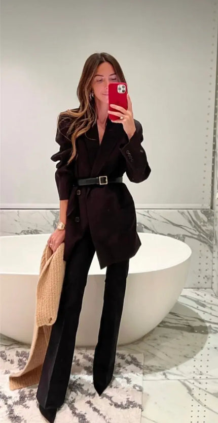 Woman wearing black belted blazer with flared pants in a modern bathroom mirror selfie