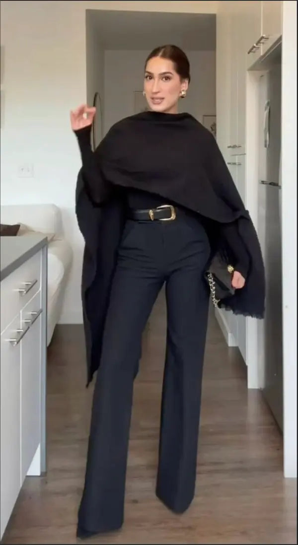 Elegant woman in black cape top and high-waisted trousers posing in modern apartment