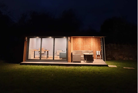 A garden office lit at nighttime with an open canopy and seating area