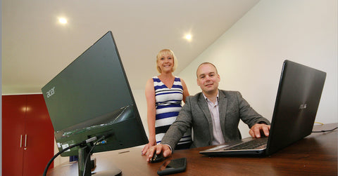 A man and woman in a garden office standing by a computer