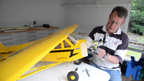 A man is working on a model airplane in his garden room studio.