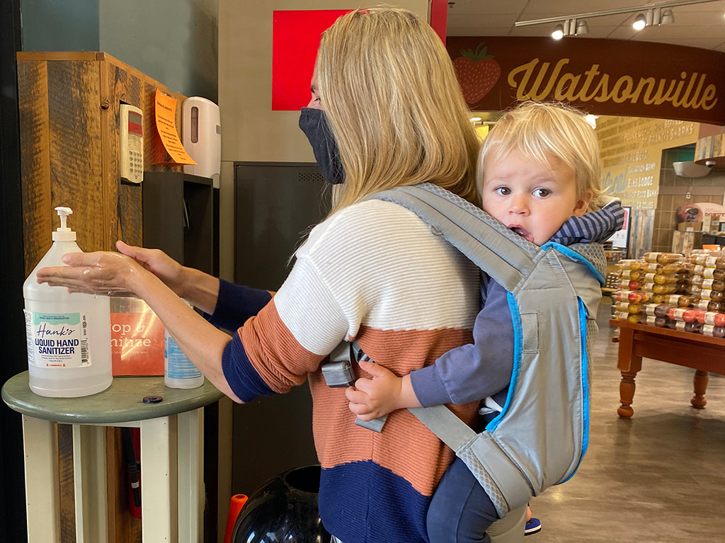 Parent sanitizing hands with baby in Onya carrier