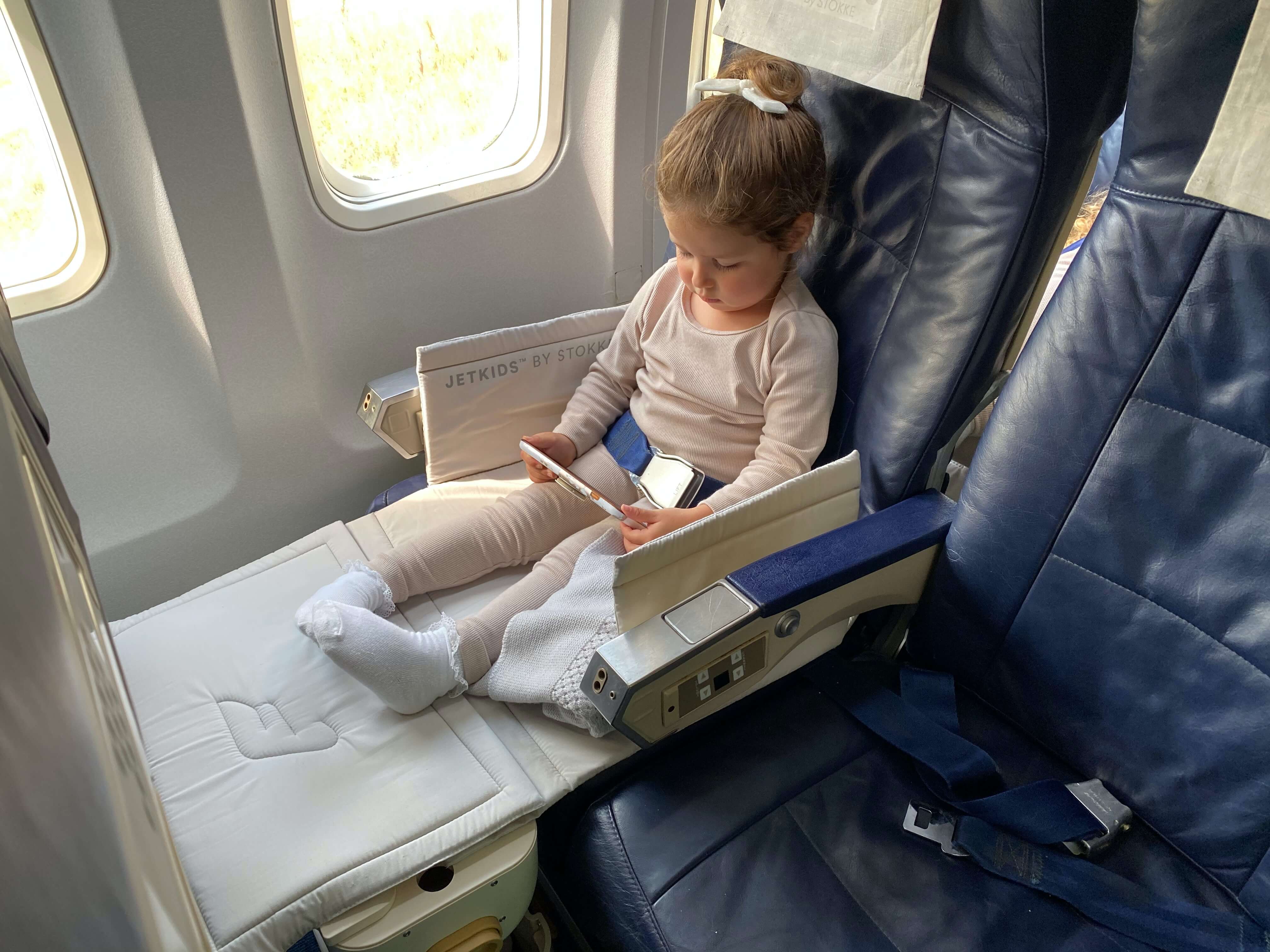 Baby sitting in an airplane seat watching a movie on a tablet