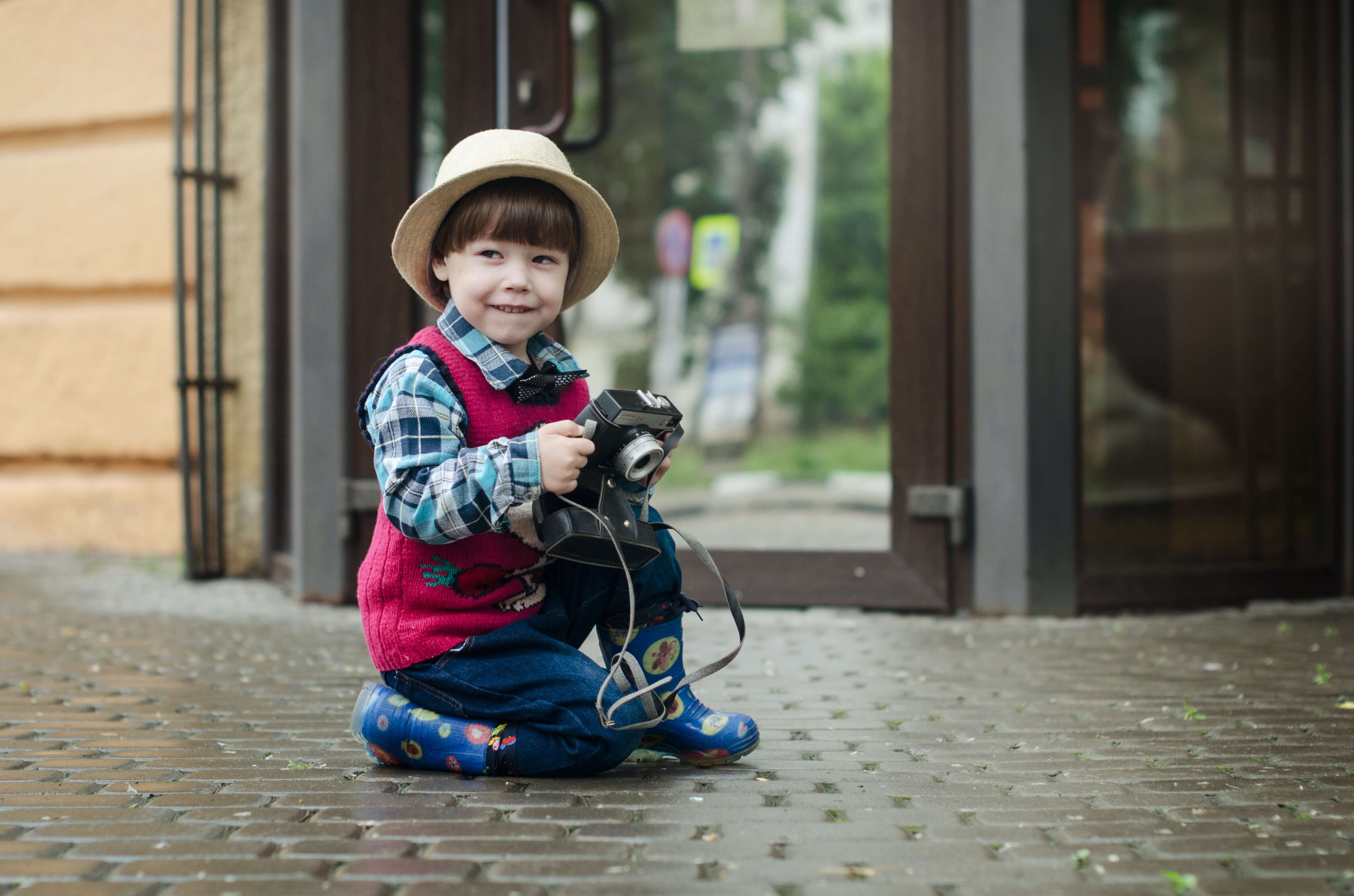 Child kneeling on ground playing with a camera and smiling