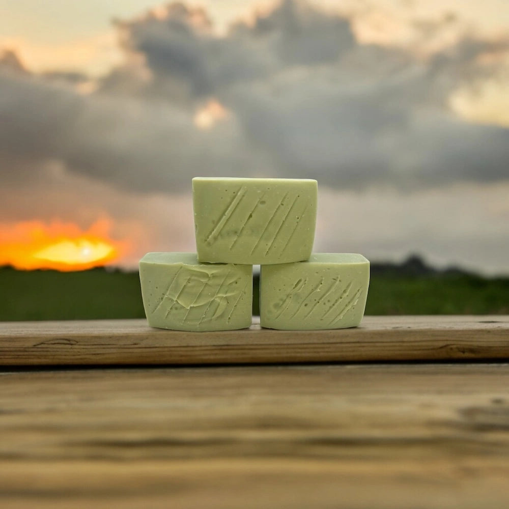 Three green soap bars stacked with a sunset in the background.