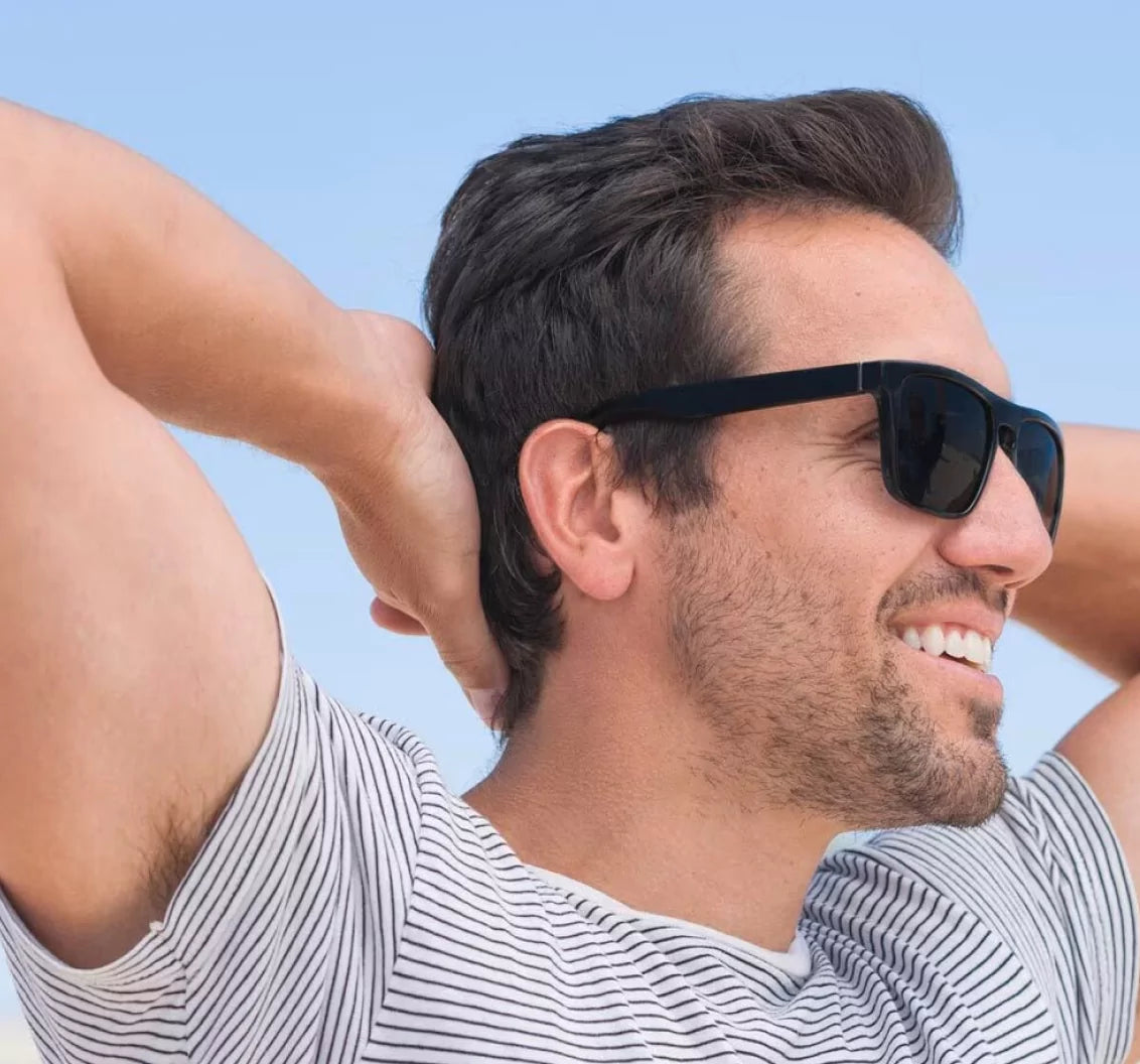 Man smiling, wearing sunglasses, and relaxing outdoors.