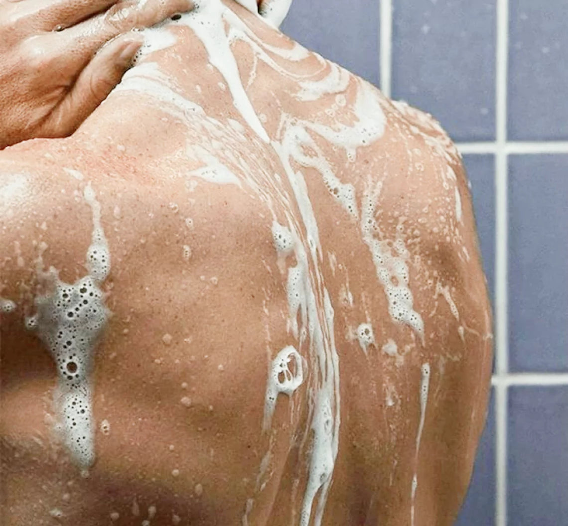 Person washing a soapy back in the shower.
