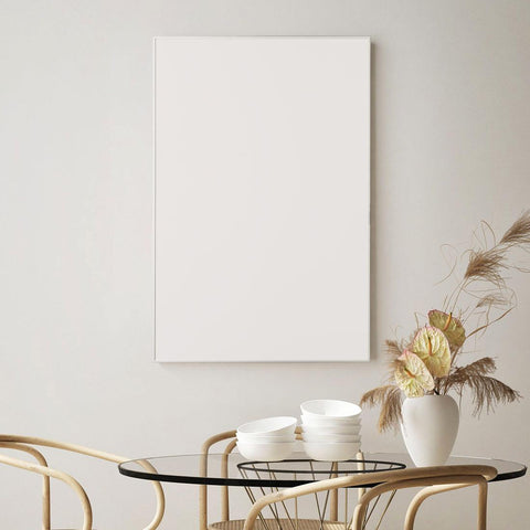 A minimalist dining area with a round glass table, light wooden chairs, and a blank canvas on the wall boasts IHS Infrared Heating Panel (905x605mm) | Framed Series | 580w for energy consumption reduction.