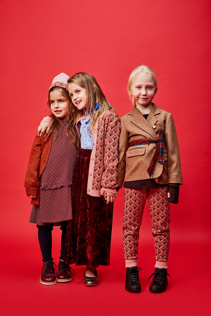 three kids standing in paade mode cardigans and dresses