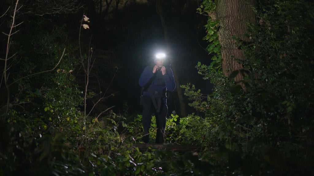Man in dark forest with surroundings illuminated by JordiLight used as headlight, highlighting the reliable outdoor lighting for adventurers.