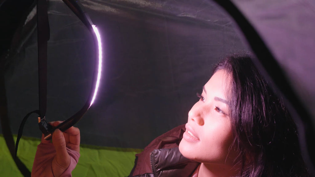 Woman in tent illuminated by JordiLight hanging overhead, showcasing the bright, reliable lighting ideal for camping adventures.