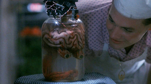 Brain with eyeballs in a jar being talked to by a man with a 50s diner uniform on from the film Blood Diner