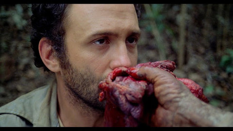 Film still from cult horror movie Cannibal Holocause showing a hand holding out human flesh in front of a man's face.