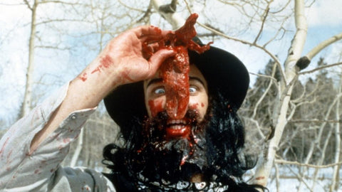 Film still from Cannibal! The Musical, featuring Trey Parker dressed as a miner holding a bloody tongue in front of his face.