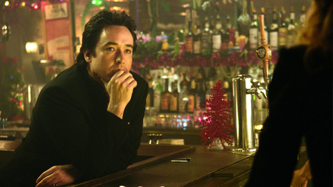 John Cusack portraying Charlie Arglist in The Ice Harvest, sitting at a bar with his hand on his chin holding a pensive expression.