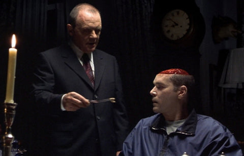 Film still from the horror movie Hannibal, showing a man with his brain exposed being fed his own brain by another man.