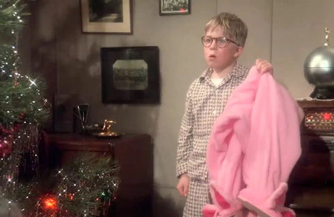 Ralphie Parker from A Christmas Story holding up a pink bunny suit while standing beside a christmas tree.