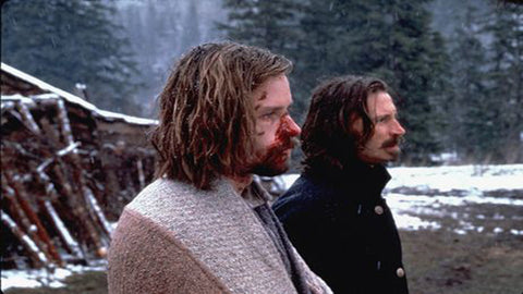 film still from the cult movie Ravenous, showing two men with bloodied faces standing side by side in a snowy woodland area.