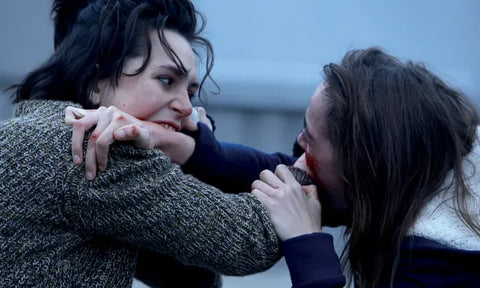 Film still from the cult horror movie Raw, showing two girls biting each others arms.
