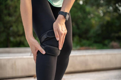 A woman holding her knee while wearing a knee brace for running.