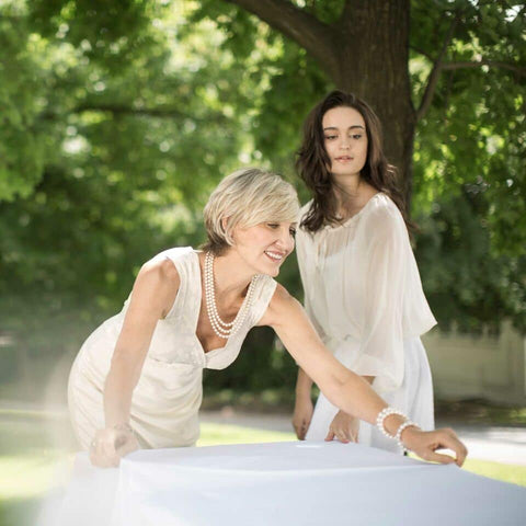 Women straightening a white tablecloth on a large dining table