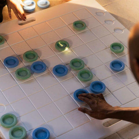 Close up of white checker board with blue and green pieces and hands moving pieces
