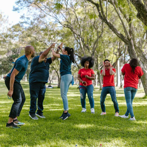 Six adults, three in teal shirts and three in red shirts. Two adults in teal shirts celebrate with their arms in the air, holding hands