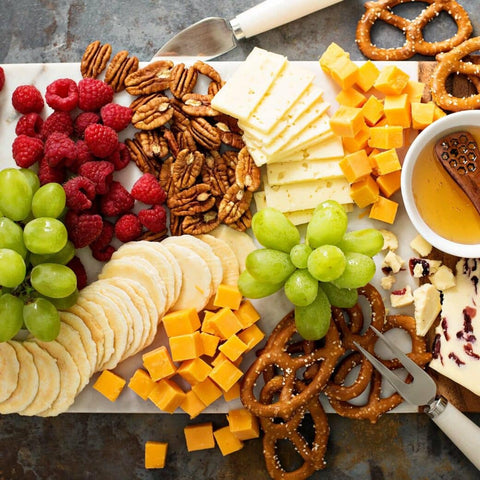 Snack platter of green grapes, raspberries, crackers, walnuts, various cheeses, and pretzels