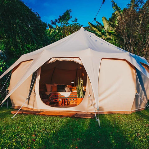 Tan tent on grass, with bed and throw pillows inside