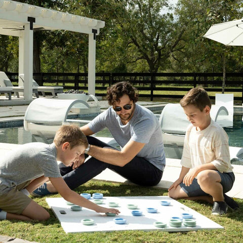Father outside on grass with kids playing checkers