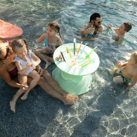 Group of children and adults in a pool eating ice pops, surrounding ice bin filled with ice and ice pops