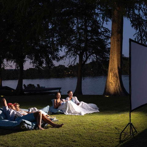 Two Ledge Lounger Laze Pillows, each with two people on it, in front of a projection screen on grass at night