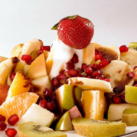 Pile of fruit salad with cut up oranges, apples, bananas, strawberries, and pomegranate perils with yogurt drizzled on top
